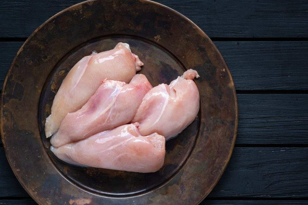 Fresh raw chicken breasts presented on an antique plate with a darker background.