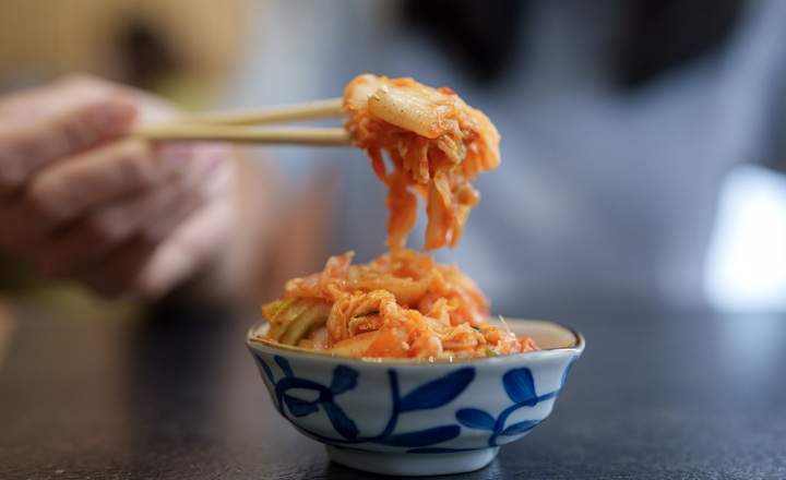 Close-up of a woman hand picking up fresh Korean kimchi from a patterned bowl using chopsticks, highlighting traditional Korean cuisine.